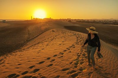 Full length of woman walking on sand against sky during sunset