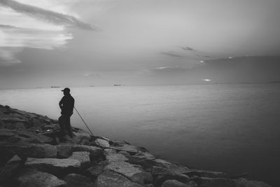 Silhouette man fishing on beach against sky