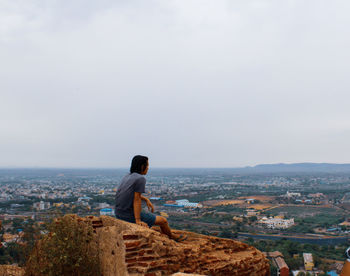 Rear view of man sitting on buildings against sky