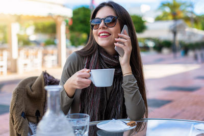 Woman talking on phone while having coffee at outdoor cafe