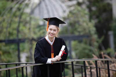 Portrait of woman wearing graduation gown against plants