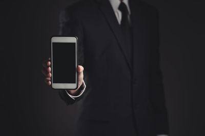 Midsection of man holding smart phone against black background