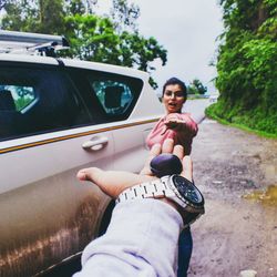 Portrait of smiling young woman sitting on car against sky