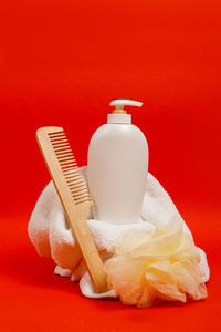 Organic shampoo in white bottle, wooden hair brush, yellow sponge, towel on bright red background