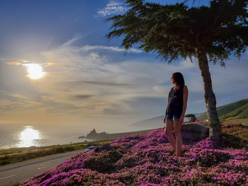 Woman standing by purple flowering tree against sky during sunset