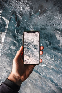 Close-up of person photographing with mobile phone in crystal clear glacier ice 
