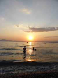 Silhouette people on beach against sky during sunset