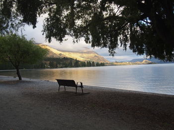 Empty chairs by lake against sky