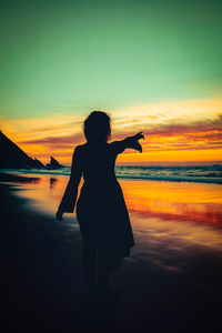 Silhouette woman standing at beach against sky during sunset