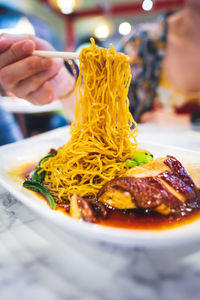 Cropped image of person holding noodles in chopsticks at table