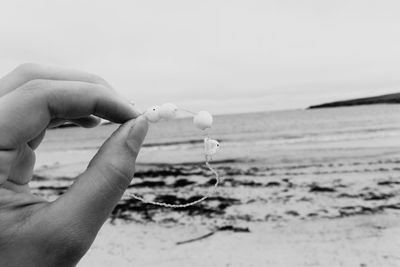 Cropped hand holding broken bracelet at beach against sky