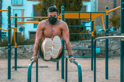 Shirtless man wearing mask exercising at park