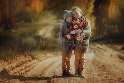 Beautiful sisters, wrapped in a warm blanket, hold a teddy bear in their hands in an autumn park