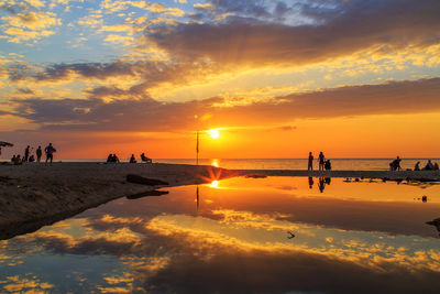 Silhouette people on beach against sky during sunset