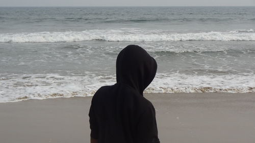 Rear view of woman standing at beach against sky