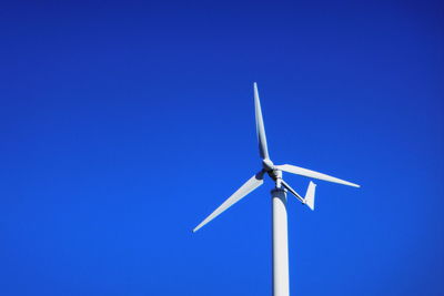 Low angle view of wind turbine against clear blue sky