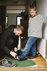 Father helping son with disability to wear shoe standing at doorway