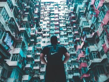 Rear view of man standing amidst buildings in city