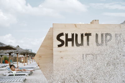 Close-up of text on wooden sign against cloudy sky