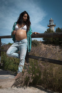 Full length of young pregnant woman standing on land against sky