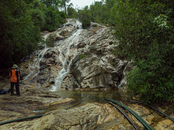 Rear view of man standing on rock against waterfall