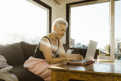 Senior woman using laptop while sitting on sofa at houseboat