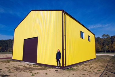 Man in the red hat stands at the wall of the iron house in nature next to the lake