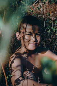 Portrait of smiling shirtless boy sitting amidst plants