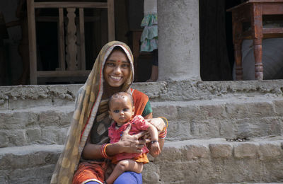 Portrait of smiling woman sitting on staircase with her child in rural india 