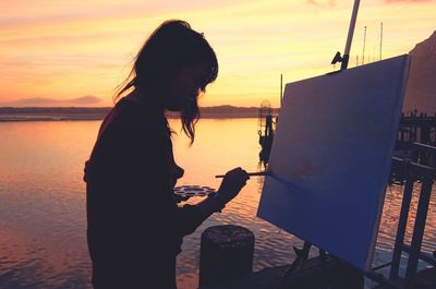 Silhouette woman standing on sea against sky during sunset