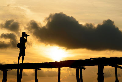 Silhouette man photographing against sky during sunset