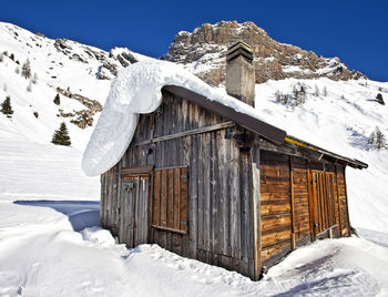 Snow covered cottage by building against sky