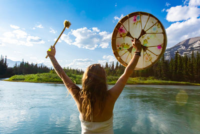 Rear view of woman holding umbrella in water against sky