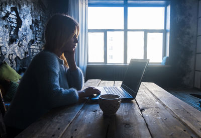 Teenage girl using laptop computer while sitting at table in home