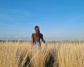 Rear view of woman standing on field against sky