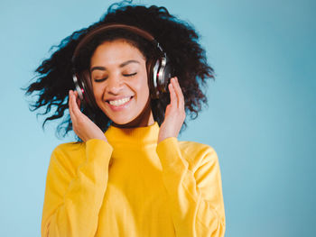 Close-up of woman enjoying music on headphones against blue background