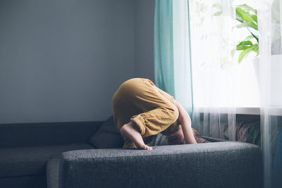 Child jumps and plays on sofa in minimalist living room, gray sofa.