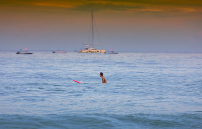 Man swimming in sea against sky during sunset