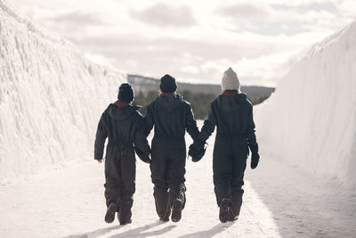 Full length rear view of mother holding hands of son and daughter while walking on snow during winter