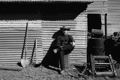 Full length of man sitting against abandoned house