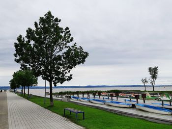 Park bench by stormy lake against sky and boats