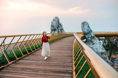 Woman standing on footbridge against sky