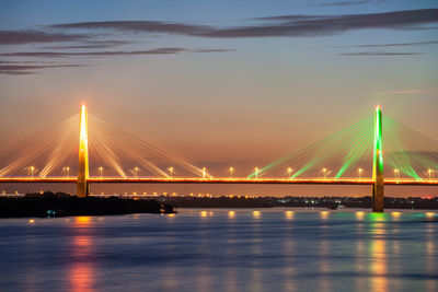 Illuminated bridge over river against sky during sunset