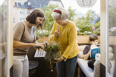 Woman and mother-in-law taking care of plant while standing in balcony