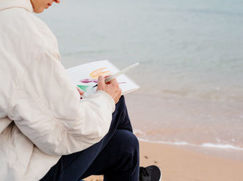 Young woman artist painting or doing travel sketches using watercolor by the seaside