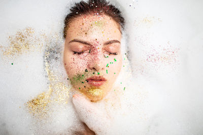 Close-up of young woman with eyes closed and glittered face in bathroom