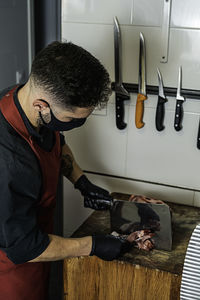 Butcher with mask cutting raw meat in the wood