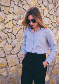 Portrait of beautiful young woman standing against brick wall