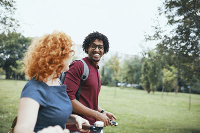 Friends walking in park, talking, woman pushing bicycle