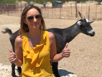 Portrait of smiling young woman gesturing while sitting against goat